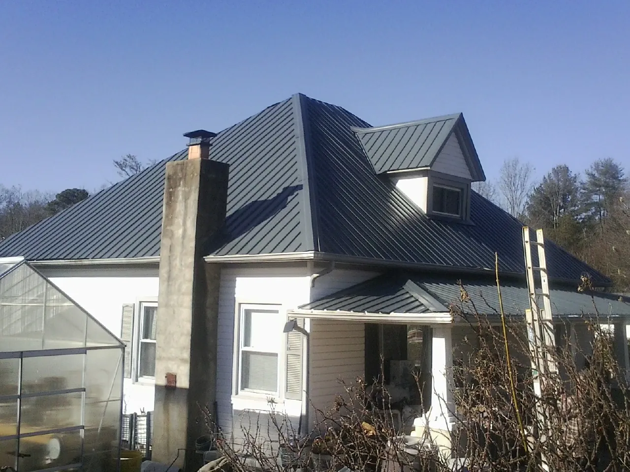 Dark blue standing seam metal roof on a white farmhouse with dormer — Slate & Tile Roof Repair by Roofing Brothers in Fontanelle