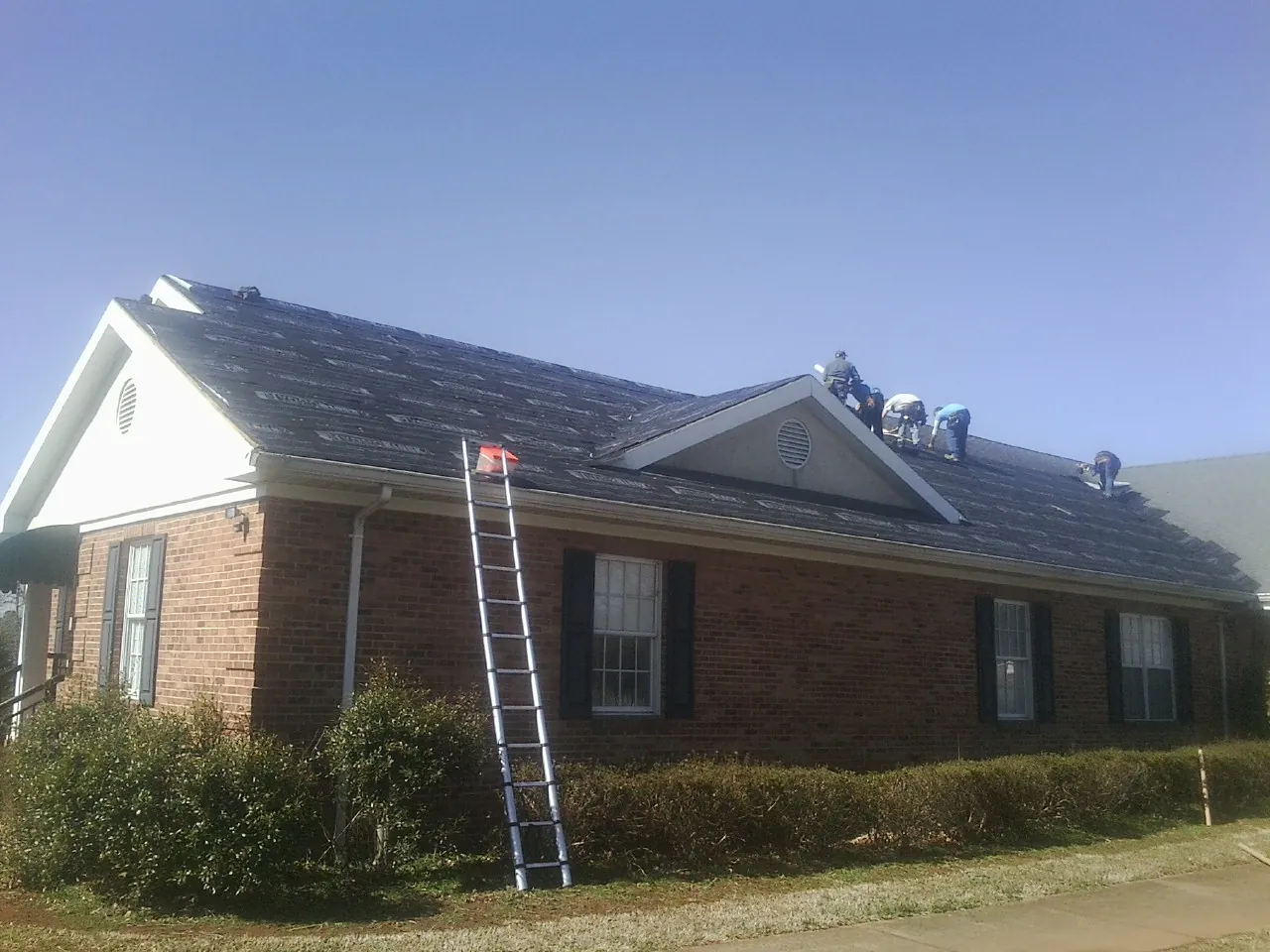 Crew tearing shingles off a brick ranch roof with a ladder set — Emergency Roof Repair work by our crew in Fontanelle