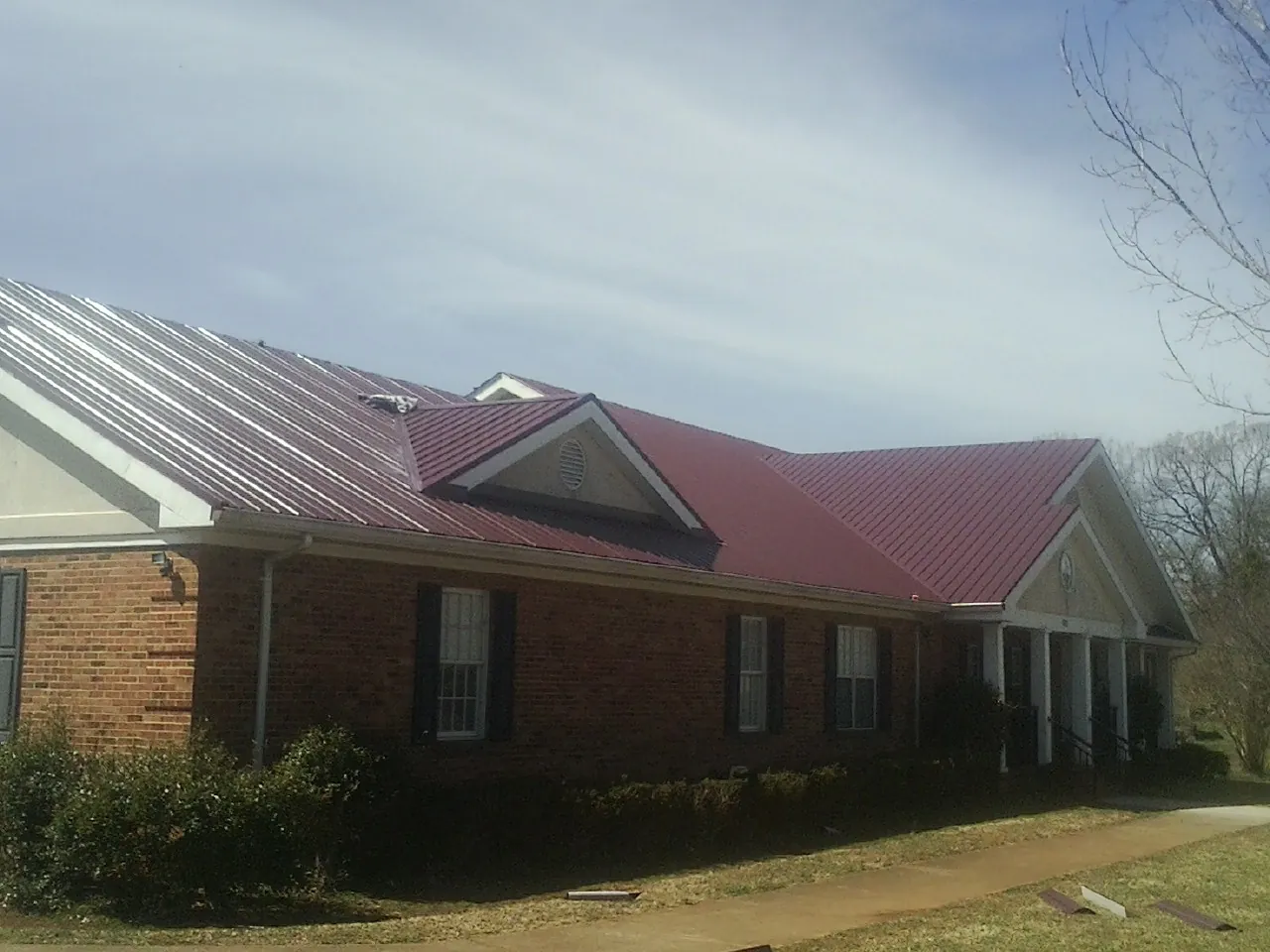 Red metal roof with gabled entries on a long brick building, from a Hail Damage Roof Repair job in Fontanelle