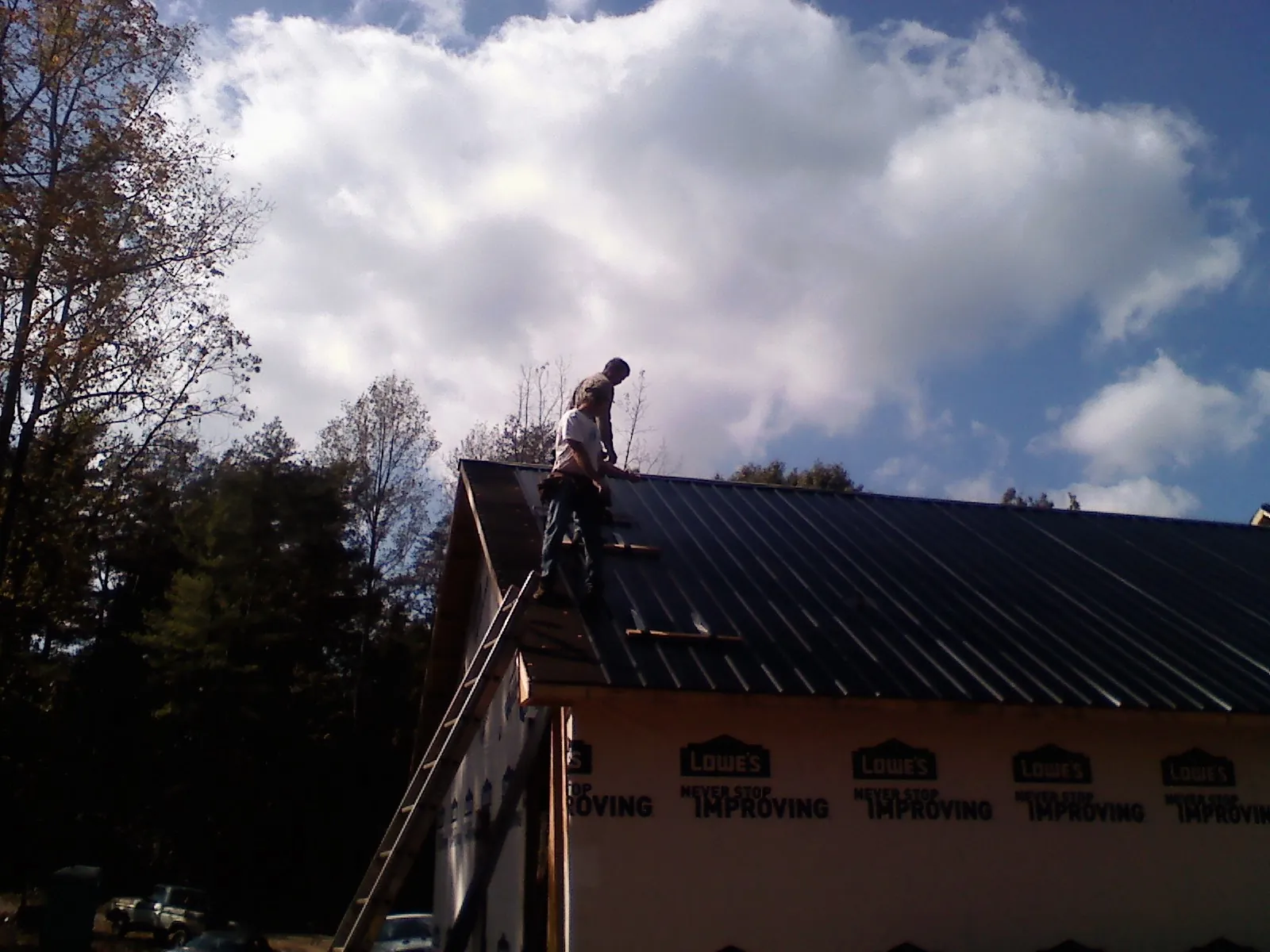 Roofer fastening dark metal panels high against a cloudy sky, from a Roof Inspection job in Fontanelle