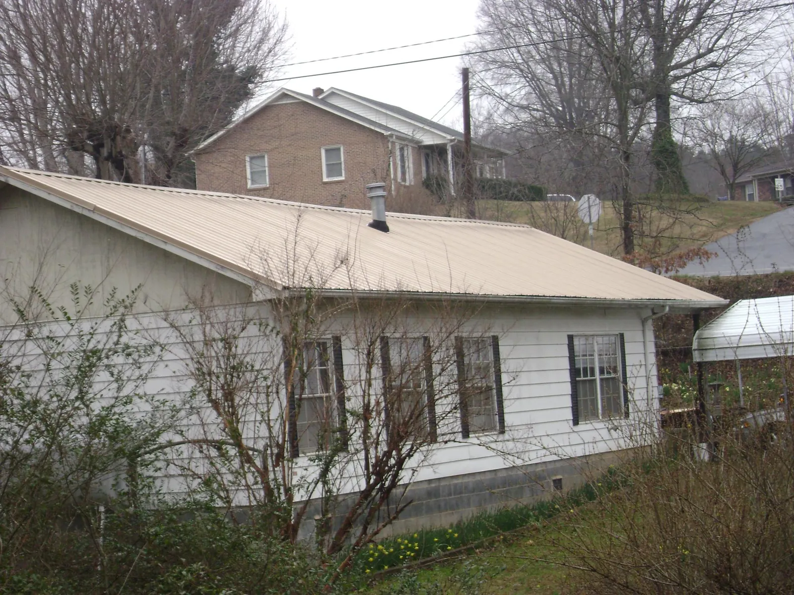 Tan metal roof on a white sided house set into a hillside — Commercial Roofing by Roofing Brothers in Fontanelle